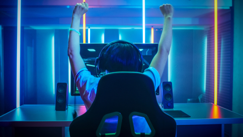 Small child sitting on a gaming chair in front of a gaming monitor with his hands in the air as if he is celebrating victory and his gifts at christmas.