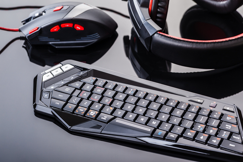 Red and black gaming keyboard, mouse and headset sitting on top of each other on a desk