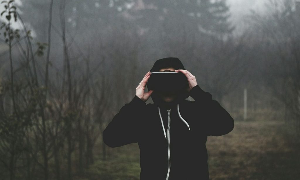 Man standing outdoors wearing a black hoodie and a Virtual Reality headset