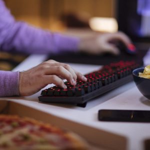 Close up shot of male hands typing on keyboard with snacks and other food within easy reach while playing games