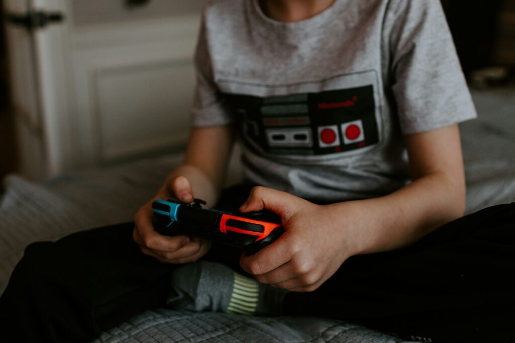 Kid sitting on grey bed while playing Nintendo Switch