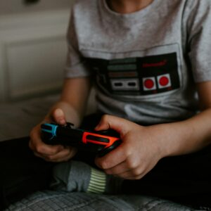 Kid sitting on grey bed while playing Nintendo Switch