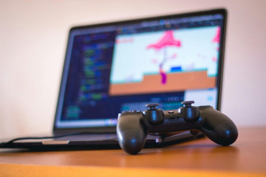 Black laptop computer beside controller on brown wooden surface as part of a game design project