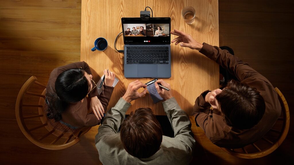 People crowded round a laptop streaming with a Hollyland Lyra 4K webcam mounted